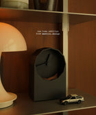 All black geometric clock sitting on a metallic shelf against a dark wood wall