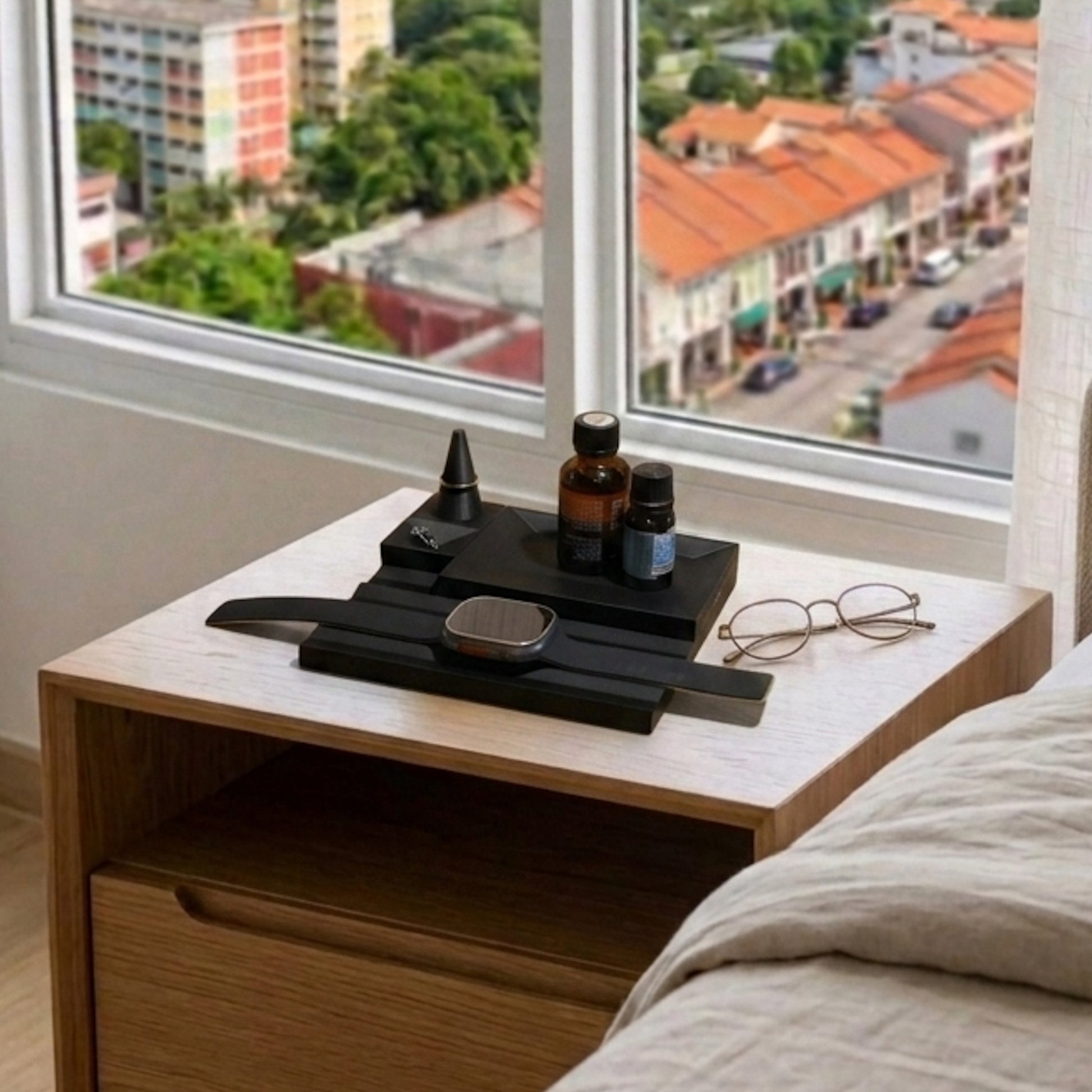 Wooden nightstand with a watch and glasses next to a window with a cityscape view.