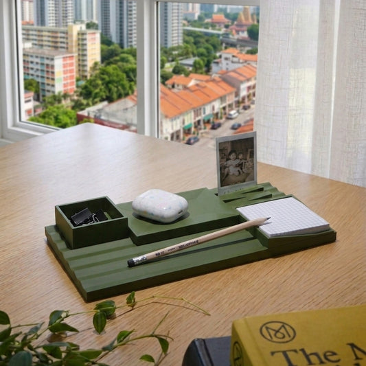 Green desk organizer with stationery items on a wooden desk with a cityscape view.