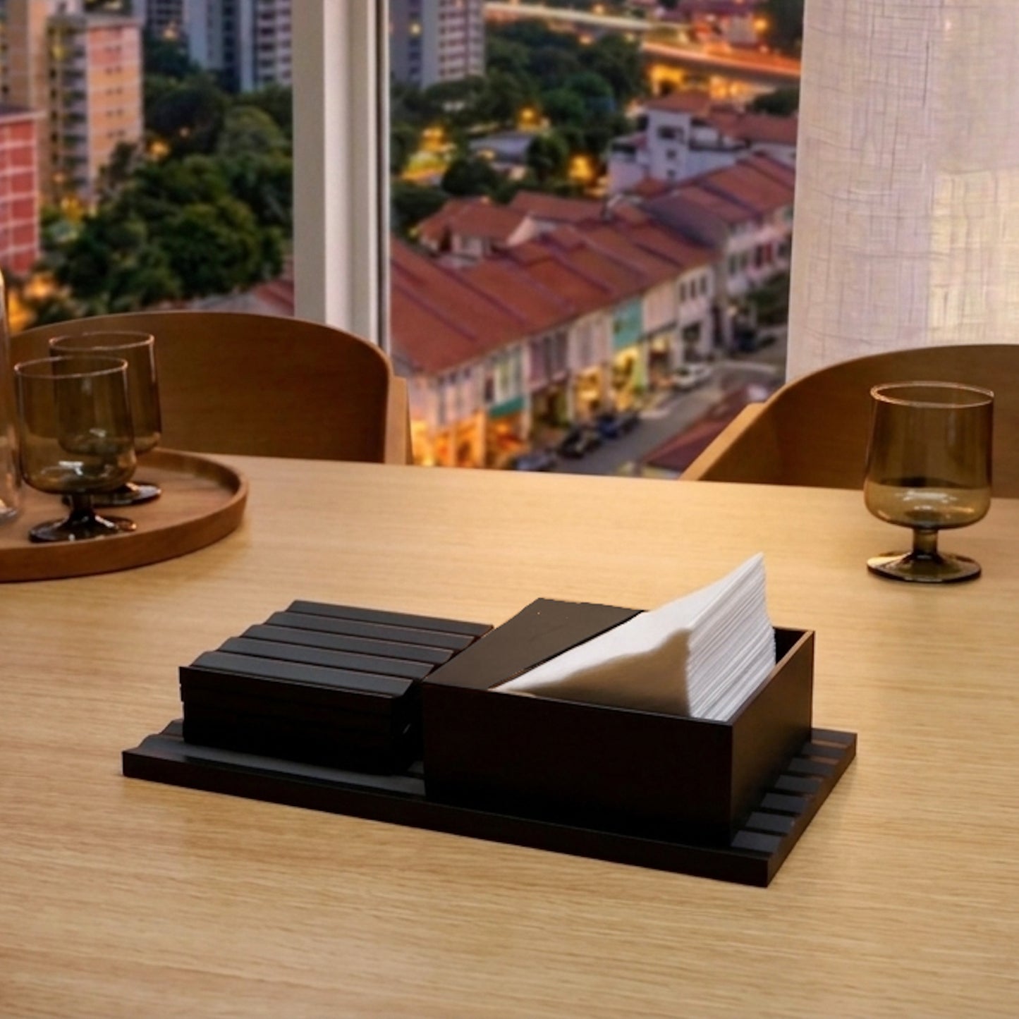 Table setting with a coasters holder and napkin holder on a wooden table, with a cityscape view in the background.